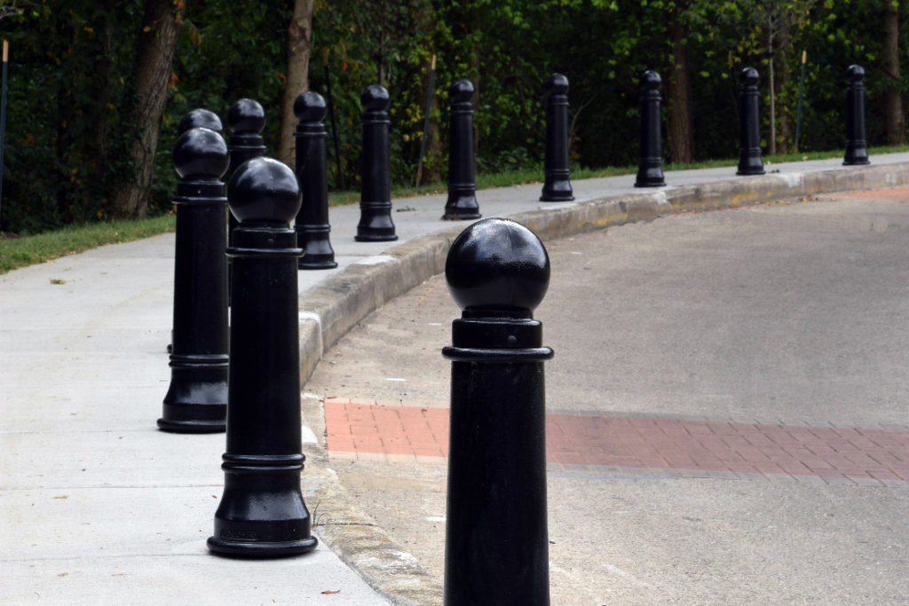 Bollards separate a sidewalk from a road beside a public park.