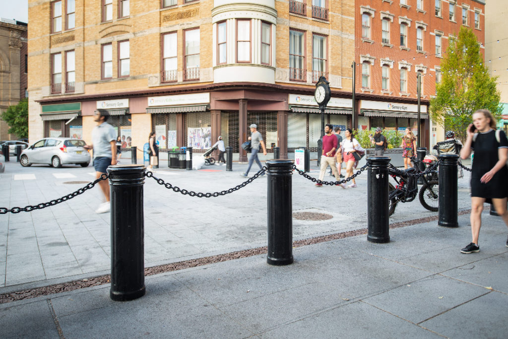 Bollards connected by chains separate pedestrian traffic in an urban setting.